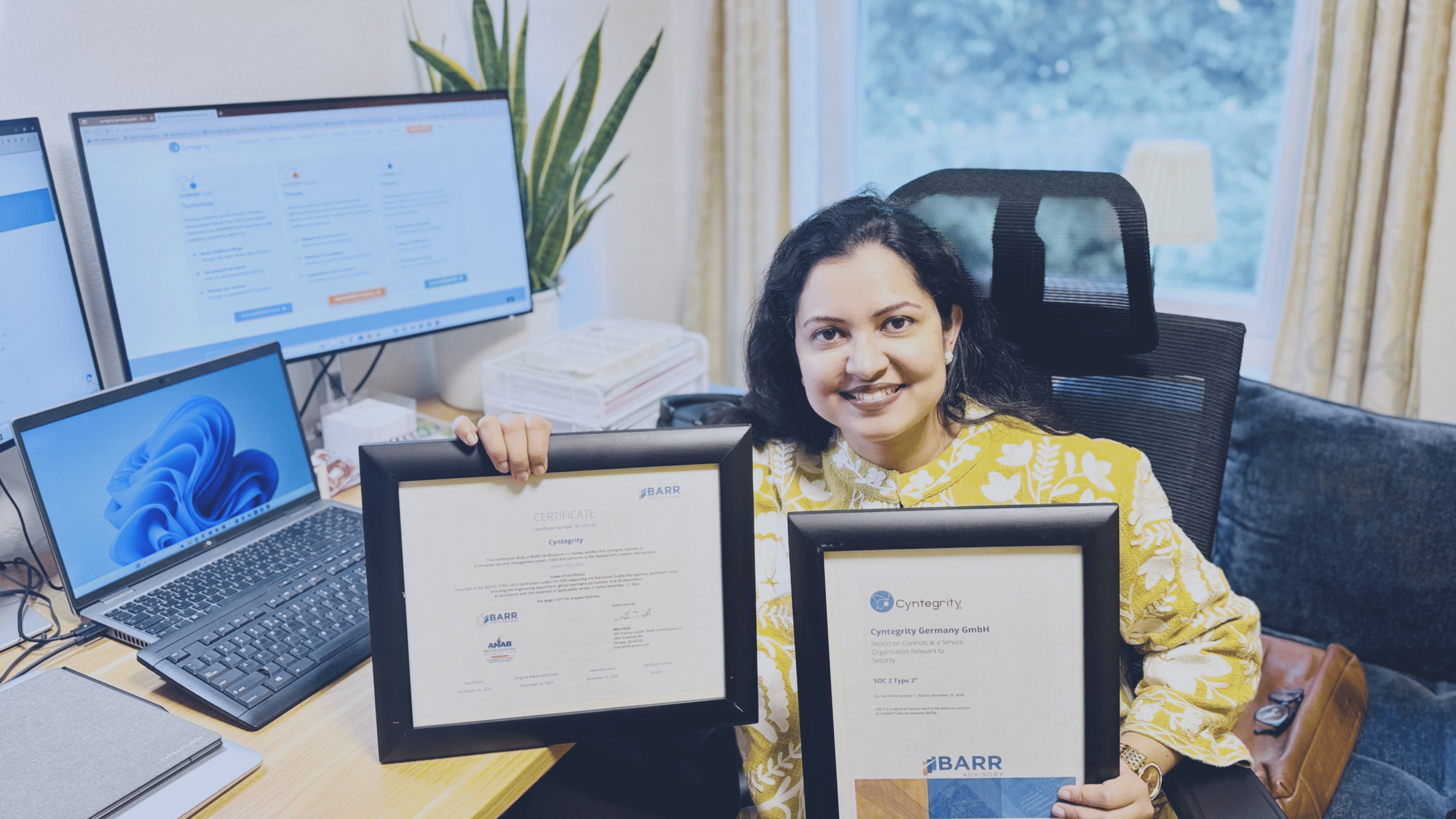 Team member holding framed compliance certificates in an office setting, highlighting regulatory and quality compliance achievements.